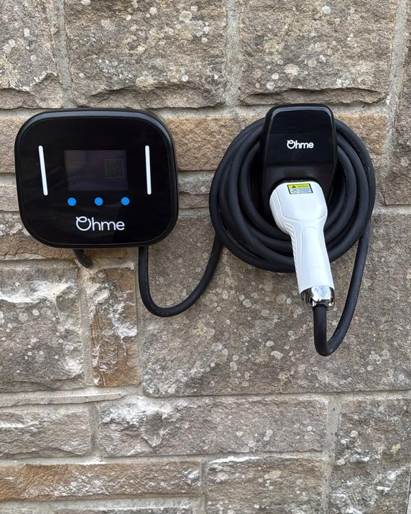 Ohme Home Pro EV charger with its tethered cable coiled on a holder, installed on a stone wall by AK Electrical